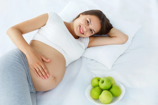 Pregnant Woman lying on the Bed with fresh Apples. Healthy Food — Stock fotografie