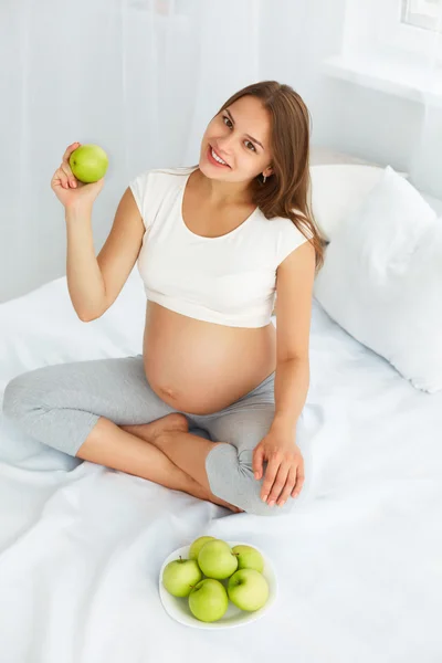 Pregnant Young Woman holding Apple while sitting on the Bed. Hea — ストック写真