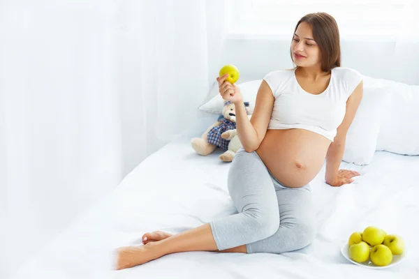 Беременная молодая женщина держит яблоко, сидя на кровати. Хеа — стоковое фото