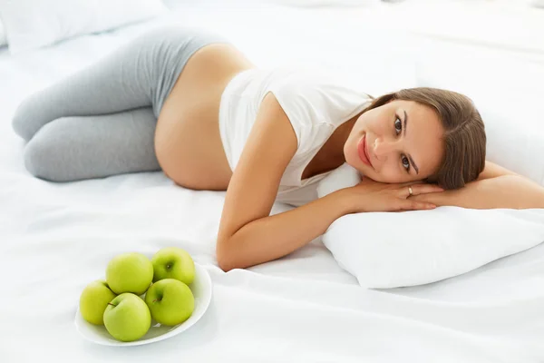 Donna incinta sdraiata sul letto con mele fresche. Cibo sano — Foto Stock