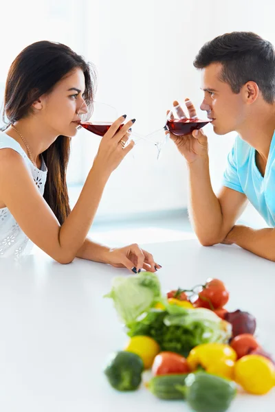 Casal olhando um para o outro enquanto bebe vinho tinto na cozinha — Fotografia de Stock