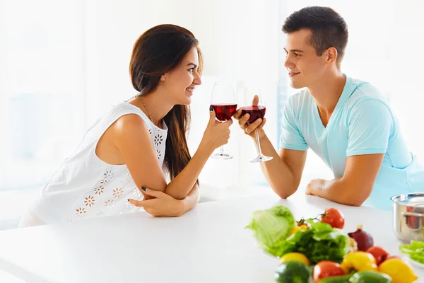 Casal sorridente com vinho e legumes na cozinha — Fotografia de Stock