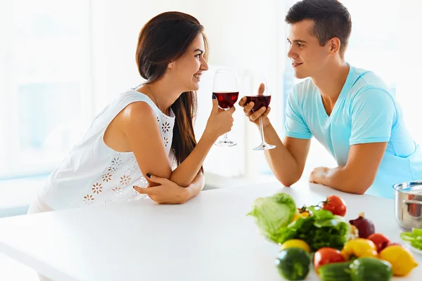 Улыбающаяся пара с вином и овощами на кухне — стоковое фото