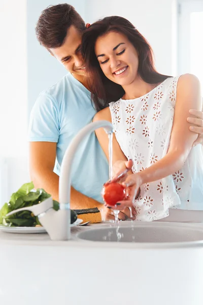 Woman washing vegetables, man hugging her  in kitchen — Stock Photo, Image