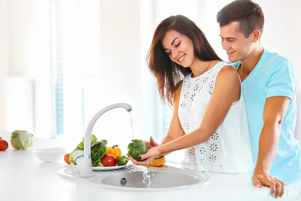 Woman washing vegetables, man hugging her  in kitchen — Stock Photo, Image