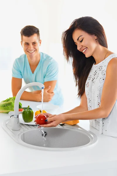 Couple washing vegetables in the kitchen. Focus on the woman. — Stock Fotó
