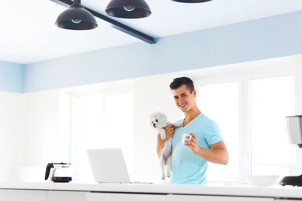 Man holding his dog, standing with a cup of coffee in the kitche — Stockfoto