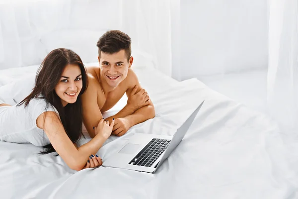 Hombre y mujer con portátil en la cama . — Foto de Stock