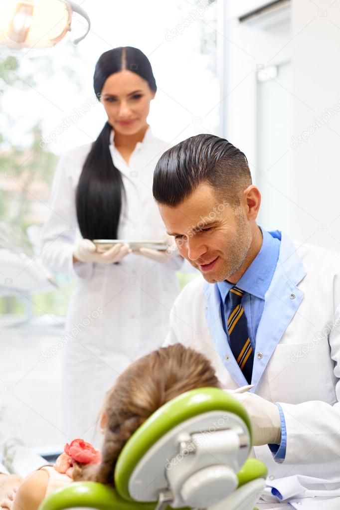 Dentist with Assistant Examining Little Girls Teeth in The Denti