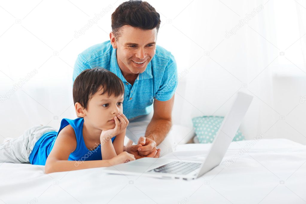 Dad and son using notebook in bedroom