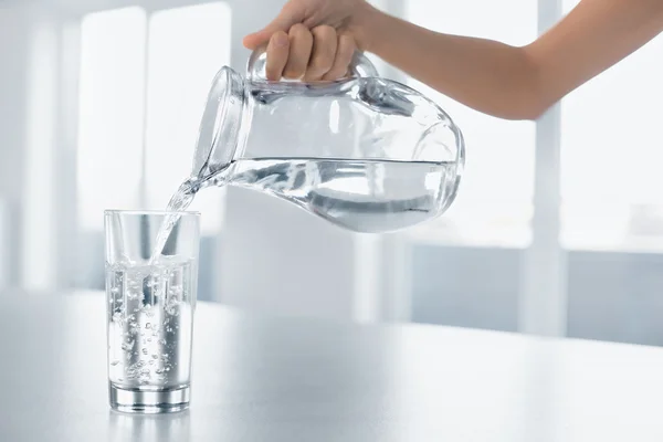 Bebe agua. La mano de la mujer vertiendo agua de la jarra en un glas — Foto de Stock