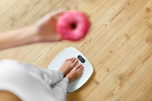 Dieta. Donna in scala di pesatura, ciambella in mano. Cibo malsano. Ob — Foto Stock