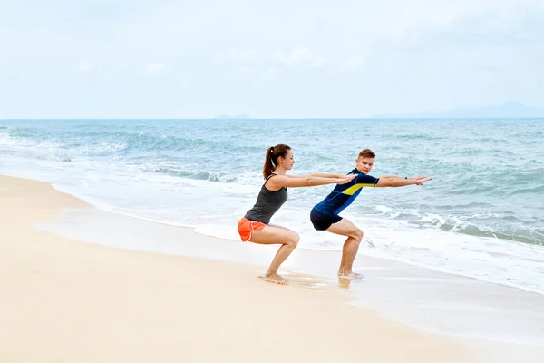 Ejercicios de fitness. Pareja sana en cuclillas, Hacer ejercicio en la playa — Foto de Stock