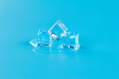 Mavi zemin üzerinde üç buz küpü eriyor, eriyen buzdan eriyen su..