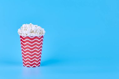 Resmin sol tarafındaki mavi arka planda patlamış mısırla dolu dalgalı bir çizgide kırmızı bir cam. Film izleme konsepti.