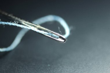 Dikiş iğnesinin makro fotoğrafı. Göz dirseğinde iplik olan küçük iğne, siyah arkaplan üzerinde izole edilmiş..