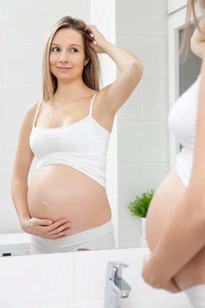 Беременная женщина в зеркале в ванной — стоковое фото