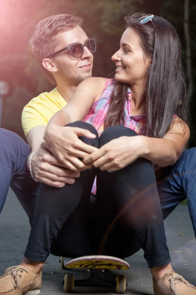 Jeune couple amoureux assis sur un skateboard en plein air — Photo