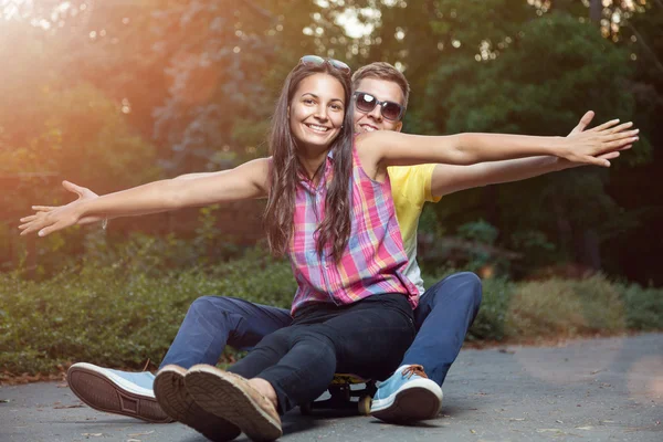 Giovane coppia innamorata seduta su uno skateboard all'aperto — Foto Stock