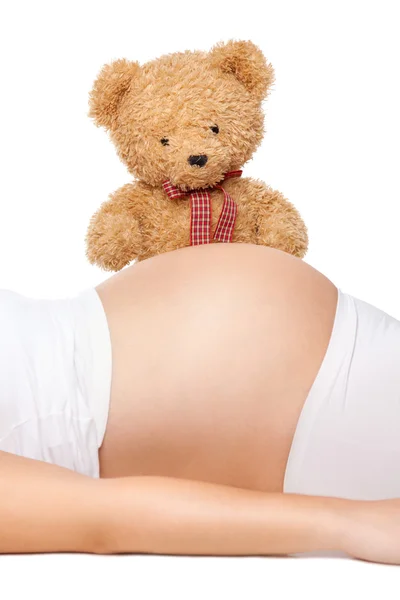 Плюшевий ведмідь дивиться на живіт вагітної жінки — стокове фото