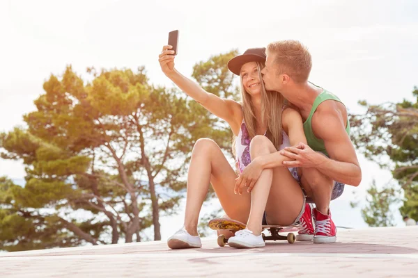 Szczęśliwa para siedzi na deskorolce i przy selfie — Zdjęcie stockowe