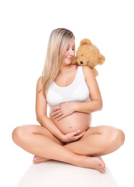 Katta oturan ve göbek tutan hamile bir kadın portresi