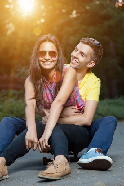 Jong paar in liefde zittend op een skateboard buitenshuis — Stockfoto