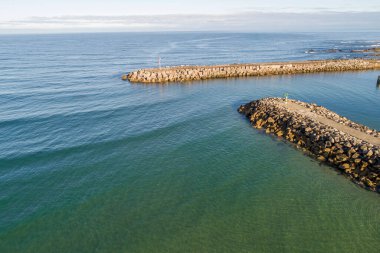 - Altı. Taş iskeleli sakin bir liman girişinin insansız hava aracı görüntüsü.