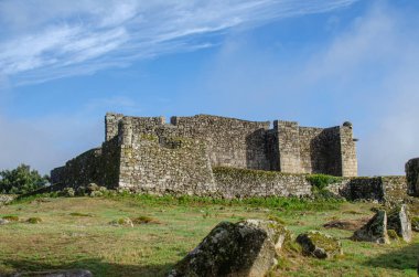 Yeşil bir tepedeki antik taş kale duvarları tarih kavramını vurguluyor..