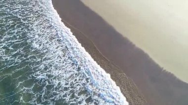 Deniz sörfünün rahatlatıcı arka planı ıssız bir sahile yuvarlanıyor.