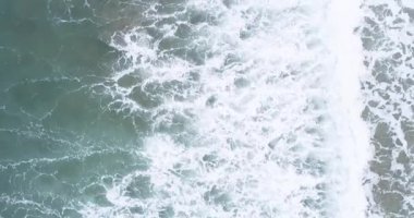 Kaba okyanus dalgalarının yukarıdan görünüşü yeşil deniz yüzeyinde beyaz köpük oluşturuyor.