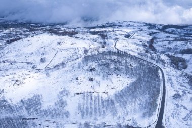 Donmuş tarlaları ve tepeleri dramatik bulutlu bir gökyüzünün altında uzak beyaz bir vadinin insansız hava aracı görüntüsü.