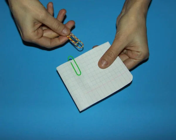 hands hold a piece of paper and fold it into two parts clamp with two paper clips