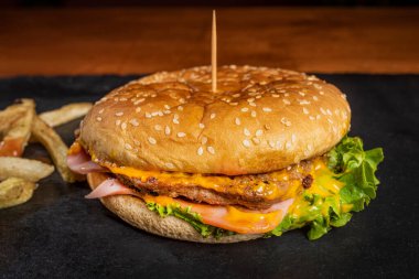 Lezzetli ve sulu bir hamburger, siyah bir arka planda, ahşap bir masada.