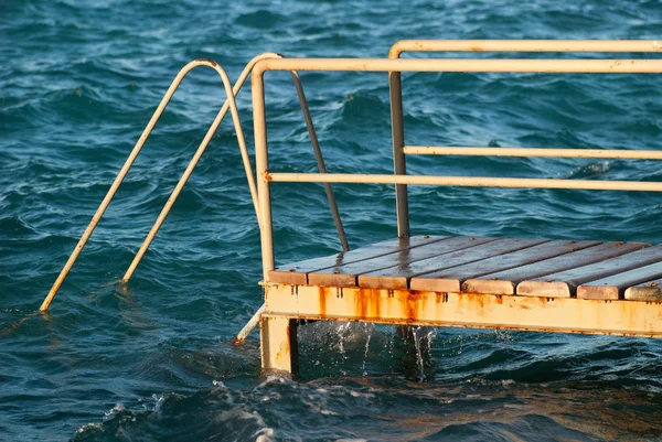 Antiguas escaleras de madera de metal vintage que conducen al agua azul turquesa del mar desde la playa. Hermoso día de verano. Piscina con grunge escaleras retro en la costa del océano. Vista lateral — Foto de Stock