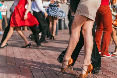 İnsanlar güneşli bir günde parkta dans ediyorlar. Ön planda, arka planda ve kırmızı etekte dans eden güzel kadın ayakları.