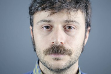 Gri arka plandaki yakışıklı genç adam kameraya bakıyor..