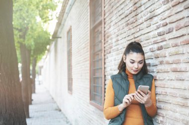 Arka plandaki beton duvarda akıllı telefon kullanan genç portresi.