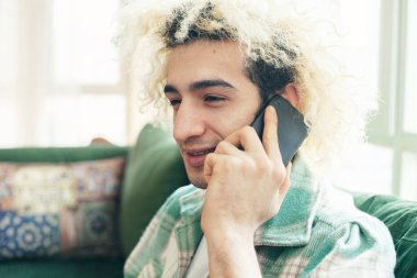 Evdeki kanepede oturan genç adam, cep telefonu kullanıyor.