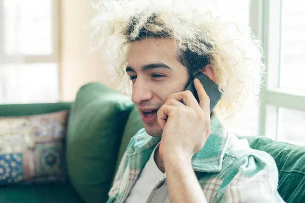 Evdeki kanepede oturan genç adam, cep telefonu kullanıyor.