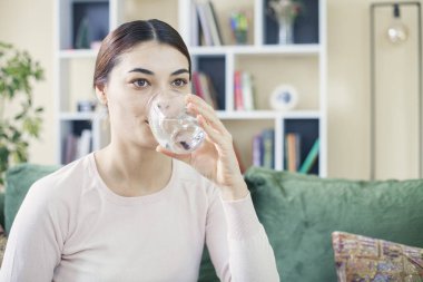 Güzel esmer kadın evdeki kanepede su içiyor.