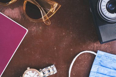 Üst görünüm seyahat konsepti retro kamera, pasaport, maske ve kahverengi arka planda gezgin güneş gözlüğü fotokopi alanı, turist gereksinimleri, klasik ton etkisi