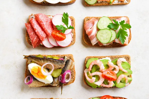 Close up view of different sandwiches with meat, vegetables, seafood over light stone background. Top view, flat lay, close up — Stock Image Close View Different Sandwiches Meat Vegetables Seafood Light Stone Background Stock Photo