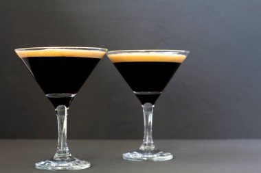 Kahve çekirdeğiyle süslenmiş espresso martini kokteyli. Siyah arka planda iki martini bardağı. Alkollü. Boşluğu kopyala.
