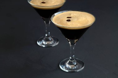 Kahve çekirdeğiyle süslenmiş espresso martini kokteyli. Siyah arka planda iki martini bardağı. Alkollü. Boşluğu kopyala.