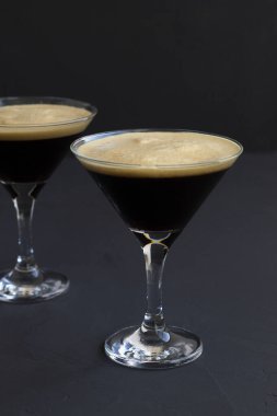 Kahve çekirdeğiyle süslenmiş espresso martini kokteyli. Siyah arka planda iki martini bardağı. Alkollü. kopyalama alanı. dikey