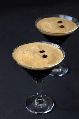 Masada kahve çekirdekleri ile süslenmiş espresso martini kokteyli. Siyah arka planda iki martini bardağı. Alkollü. kopyalama alanı. dikey