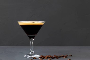 Masada kahve çekirdekleri ile süslenmiş espresso martini kokteyli. Siyah arka planda kahverengi kahve çekirdekli martini bardağı. Alkollü. Boşluğu kopyala