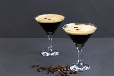 Kahve çekirdeğiyle süslenmiş espresso martini kokteyli. Siyah arka planda iki martini bardağı. Alkollü. Boşluğu kopyala.