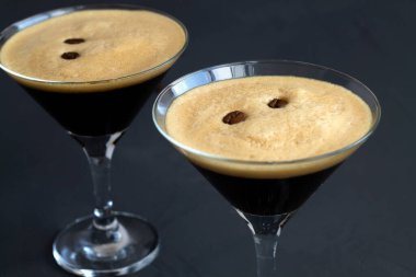 Kahve çekirdeğiyle süslenmiş espresso martini kokteyli. Siyah arka planda iki martini bardağı. Alkollü. Boşluğu kopyala.